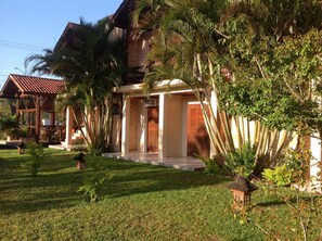 A house with a brick exterior, a wooden deck, and a well-maintained lawn. - Pousada A Cabana (Garopaba)