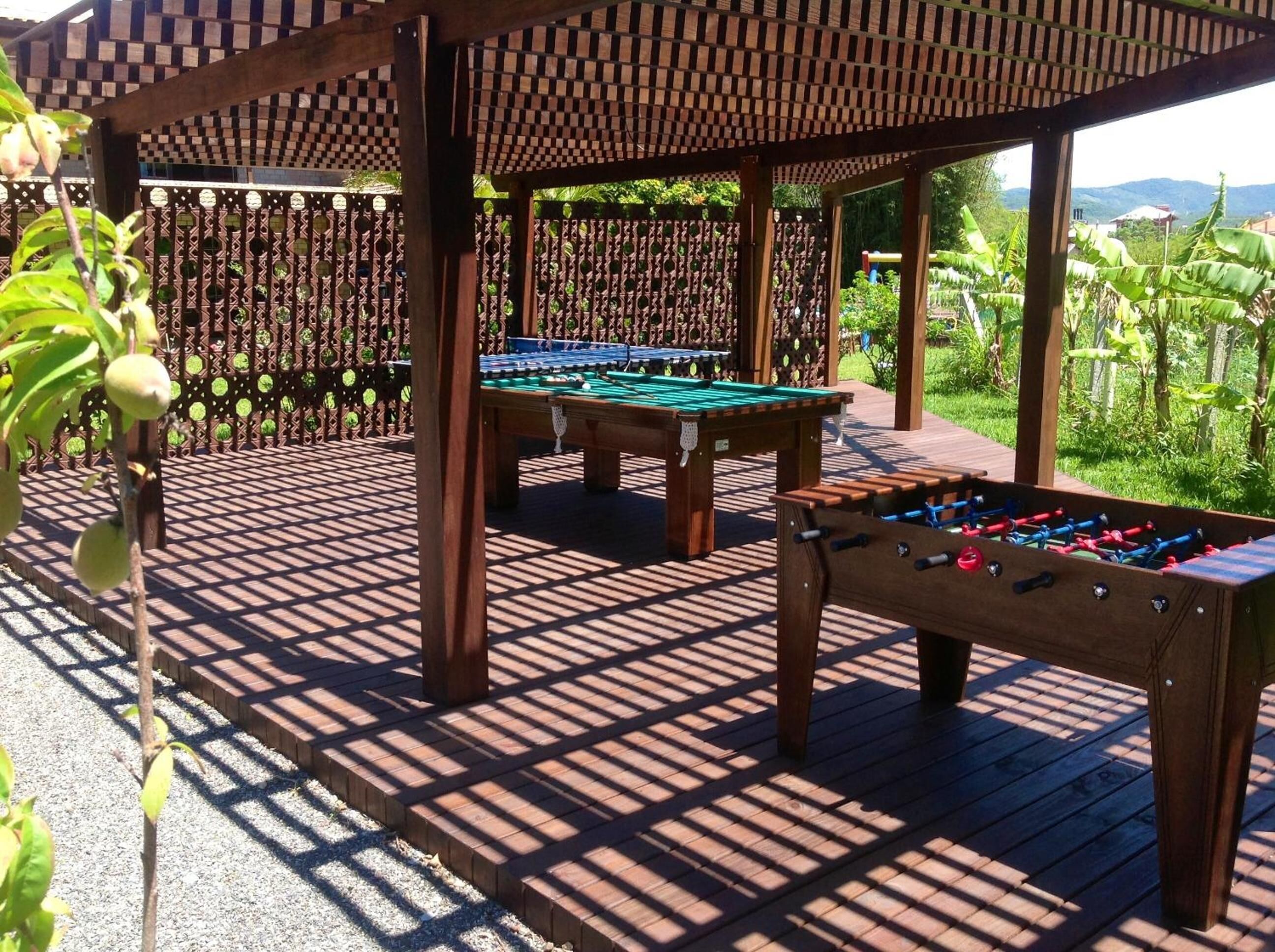 Un espacio recreativo al aire libre con mesa de billar y mesa de fútbolín bajo una pérgola de madera.