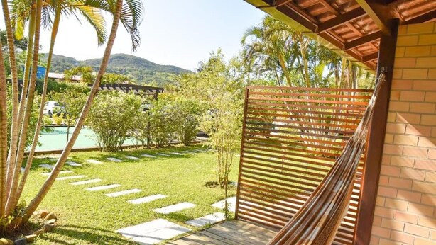 Una hamaca bajo un pérgola de madera con vista a una piscina y un jardín exuberante.