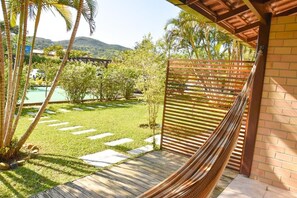 A hammock under a wooden pergola with a view of a pool and a lush garden. - Pousada A Cabana (Garopaba)