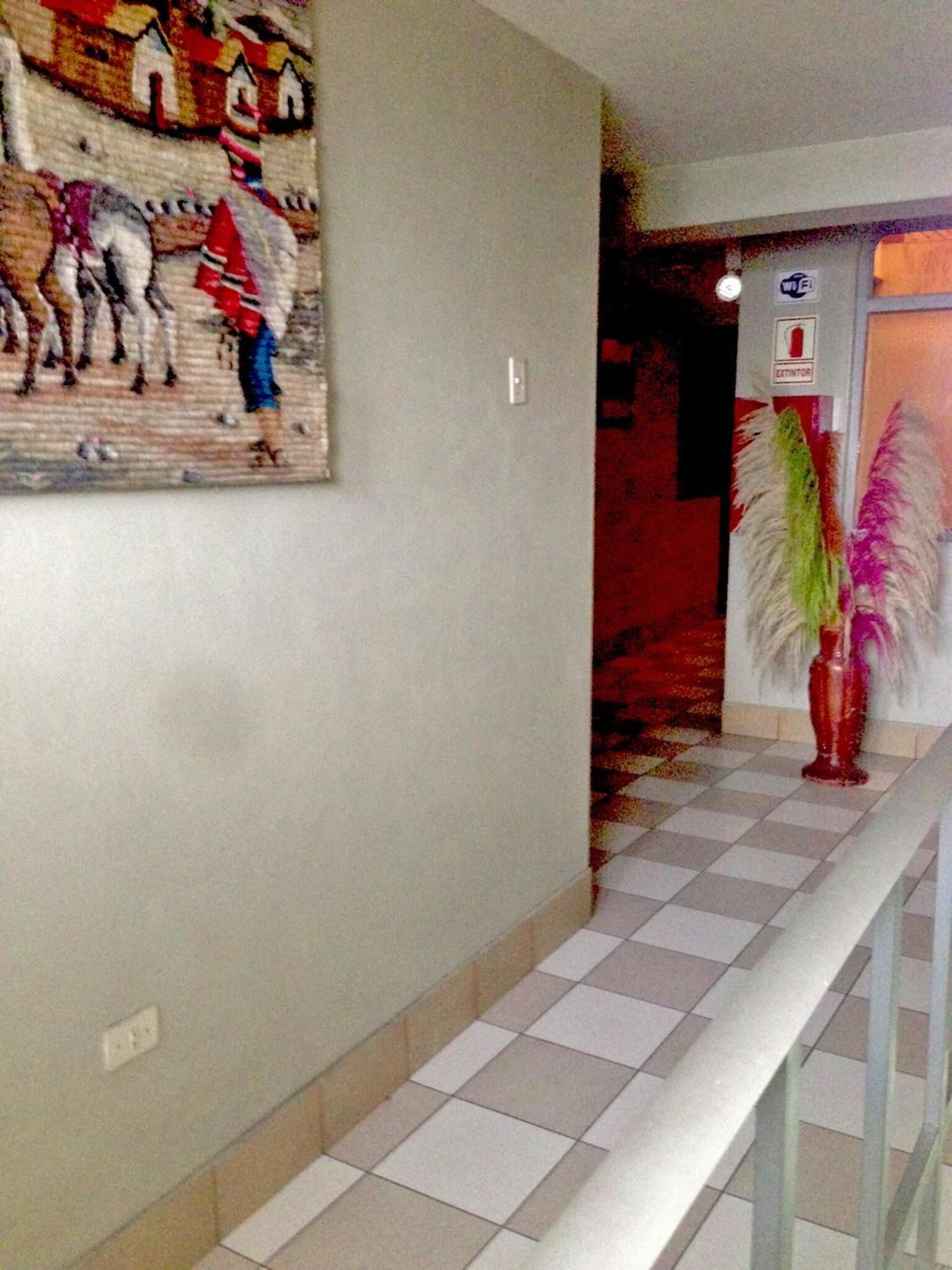 Un pasillo con piso de baldosas, un aplique en la pared y una puerta con símbolo de Wi-Fi.