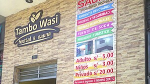 Un hotel llamado 'Tambo Wasi' con un cartel que anuncia servicios como sauna, medicina herbal y vistas de la ciudad. Se muestran los precios para adultos, niños y habitaciones privadas.