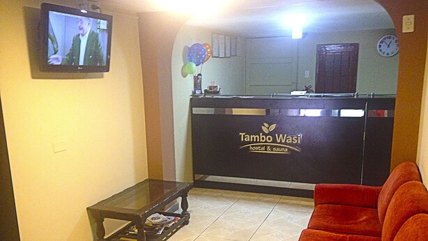 Un área de recepción con un sofá, un televisor y un mostrador de recepción con el rótulo 'Tambo Wasi'.
