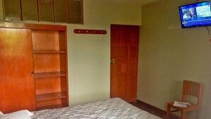 Un dormitorio con cama, armario de madera, puerta y televisor en la pared.
