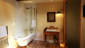 A bathroom with a freestanding bathtub, a wooden vanity with a sink, and a shower area with tiled walls. - The Cross Keys (Saffron Walden)