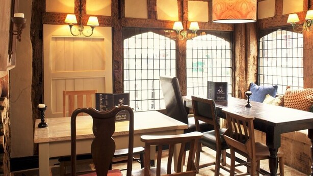 A rustic dining area with wooden beams, a table, chairs, and a chandelier. - The Cross Keys (Saffron Walden)