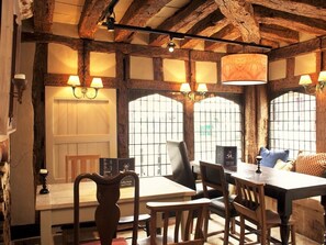 Un coin repas rustique avec des poutres en bois, une table, des chaises et un lustre.