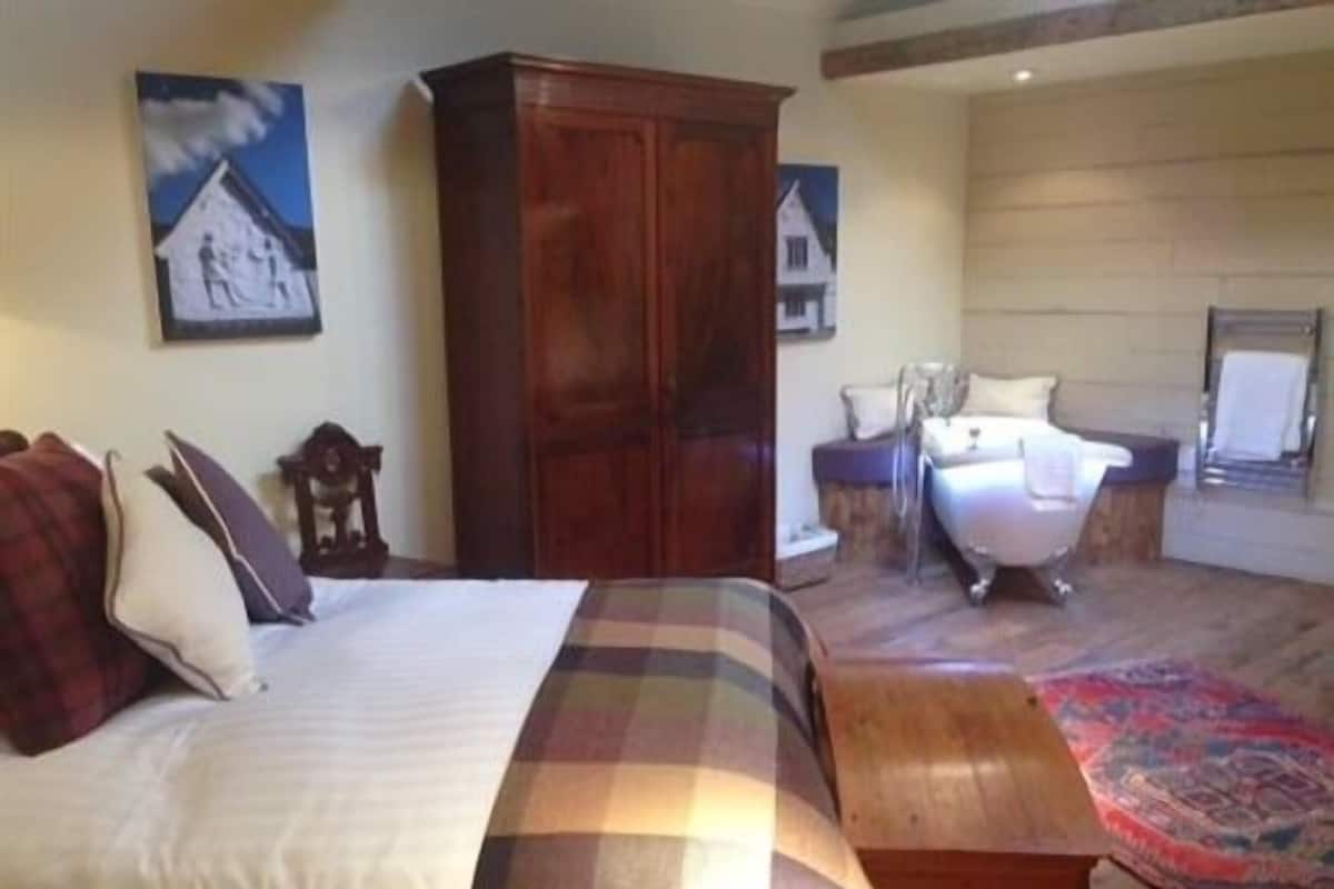 A bedroom with a bed, a wooden wardrobe, a nightstand, a chair, and a large rug.