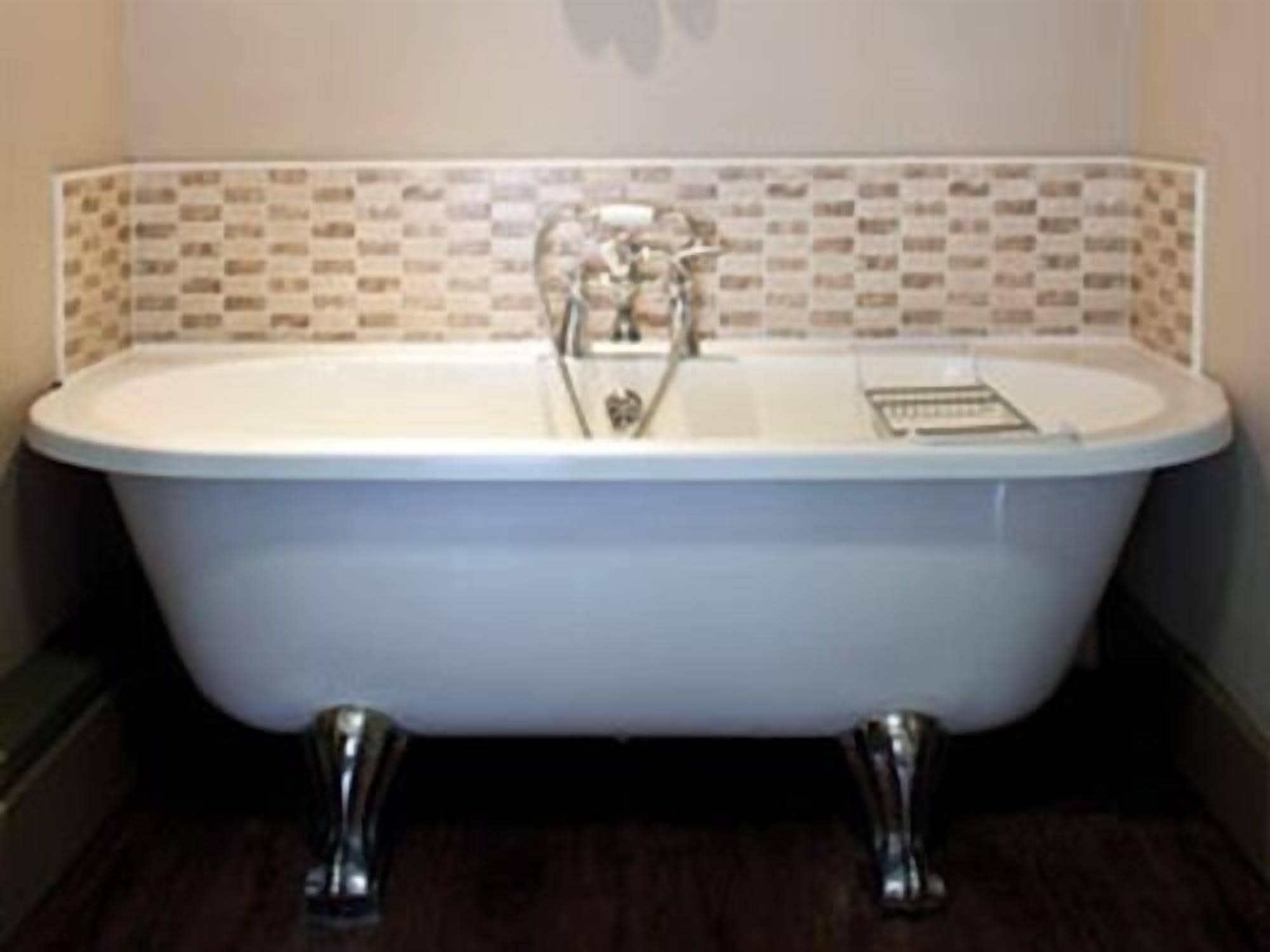 A freestanding bathtub with a white basin and chrome fixtures, set against a tiled wall.