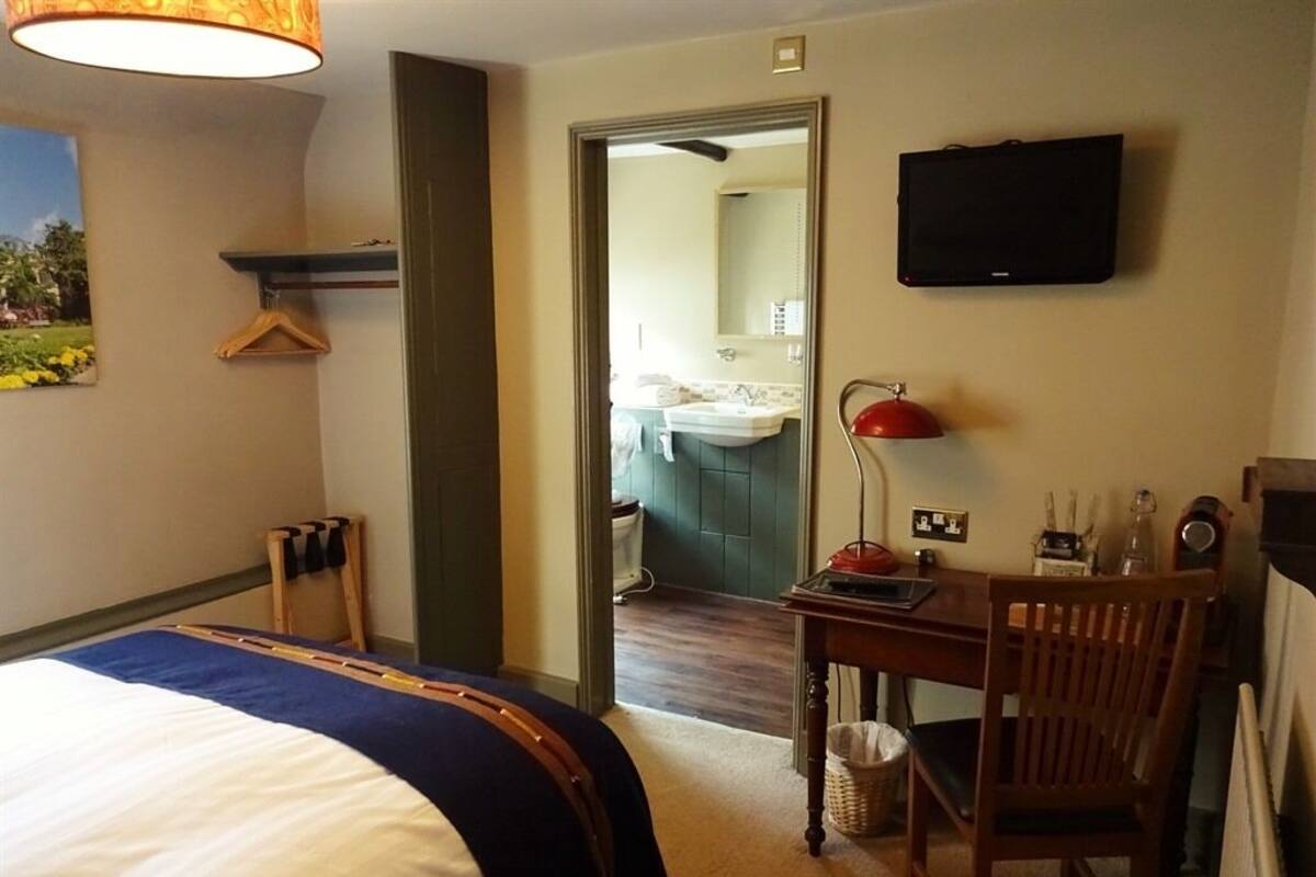 A hotel room with a bed, a desk, a chair, a television, and a bathroom visible through an open door.