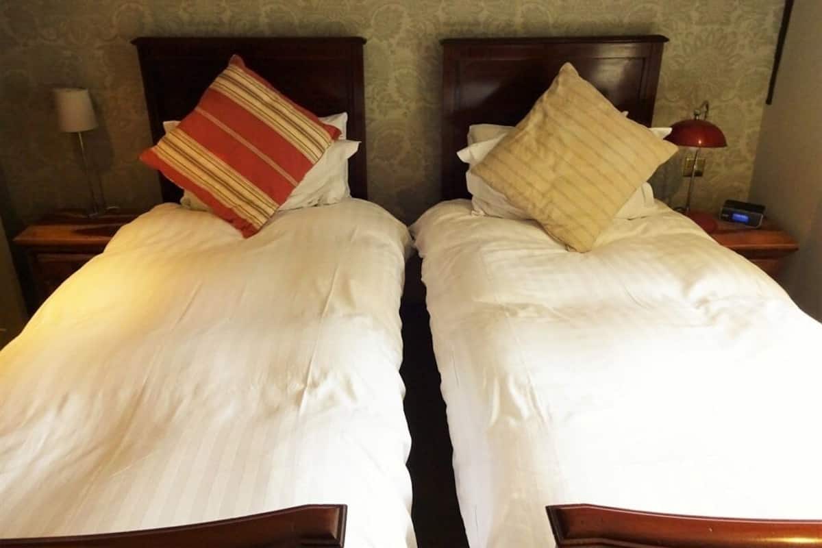 Two single beds with wooden headboards, white bedding, and a red lamp on the nightstand.
