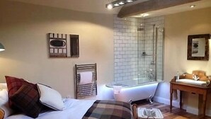 A bedroom with a bed, a bedside table, a mirror, a shower area, and a wooden floor. - The Cross Keys (Saffron Walden)