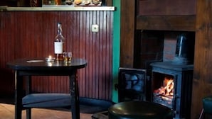 A bar area with a wooden table and a stool, a bottle of liquor, and a fireplace with a visible fire. - The Hopetoun Arms Hotel (Biggar)