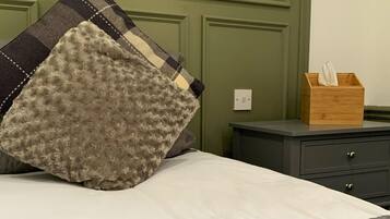 A bed with a white sheet and a textured pillow, a bedside table with a tissue box, and a green headboard.