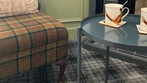 A plaid armchair with a cushion, a small round table with two white mugs with bird designs, and a black fireplace. - The Hopetoun Arms Hotel (Biggar)