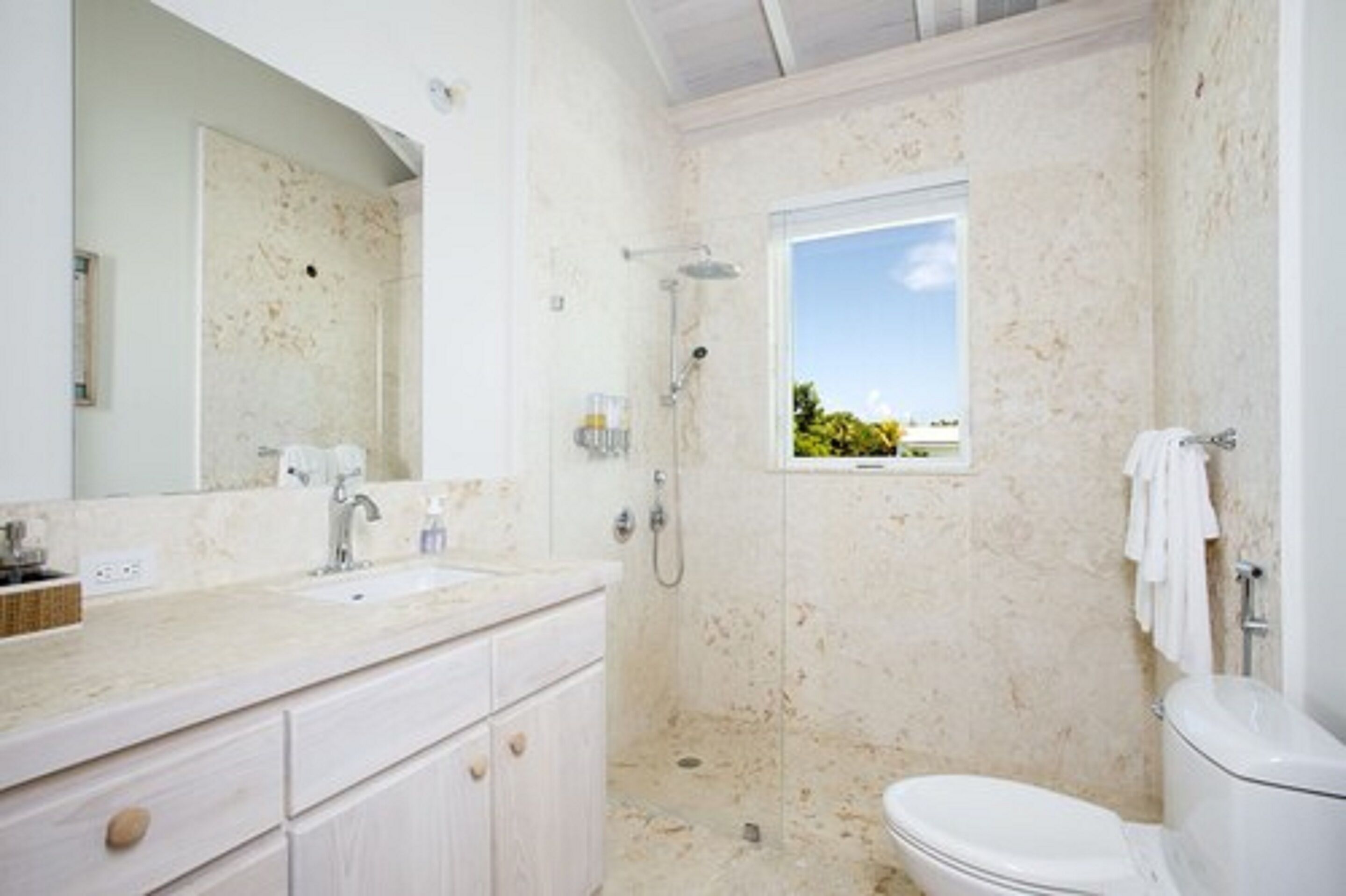 A bathroom with a large mirror, a sink, a shower, and a toilet.