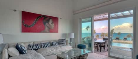 A modern living room with a glass coffee table, a white sofa with patterned cushions, and a large painting on the wall.