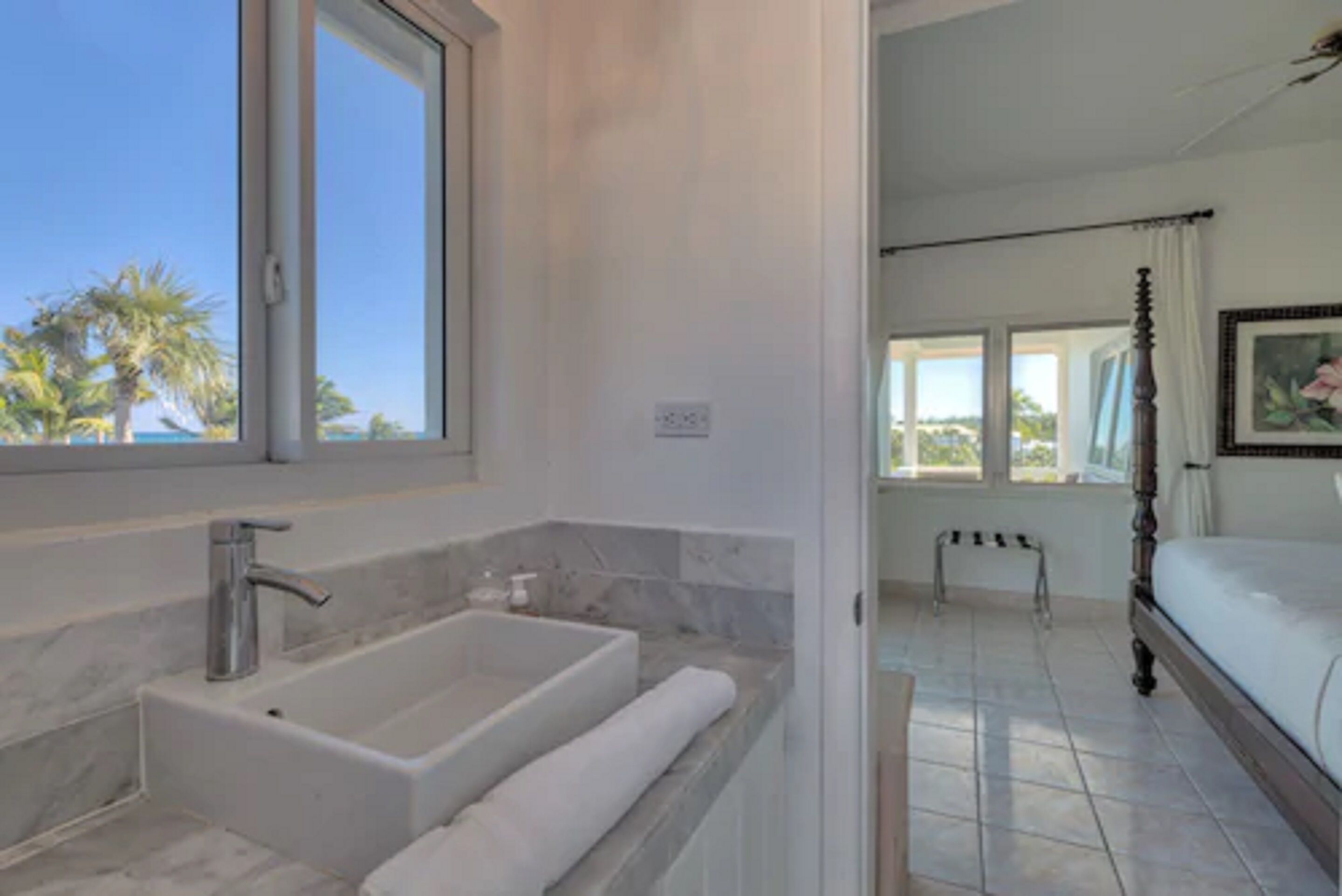 A modern bathroom with a large bathtub, a shower, and a window offering a view of palm trees.