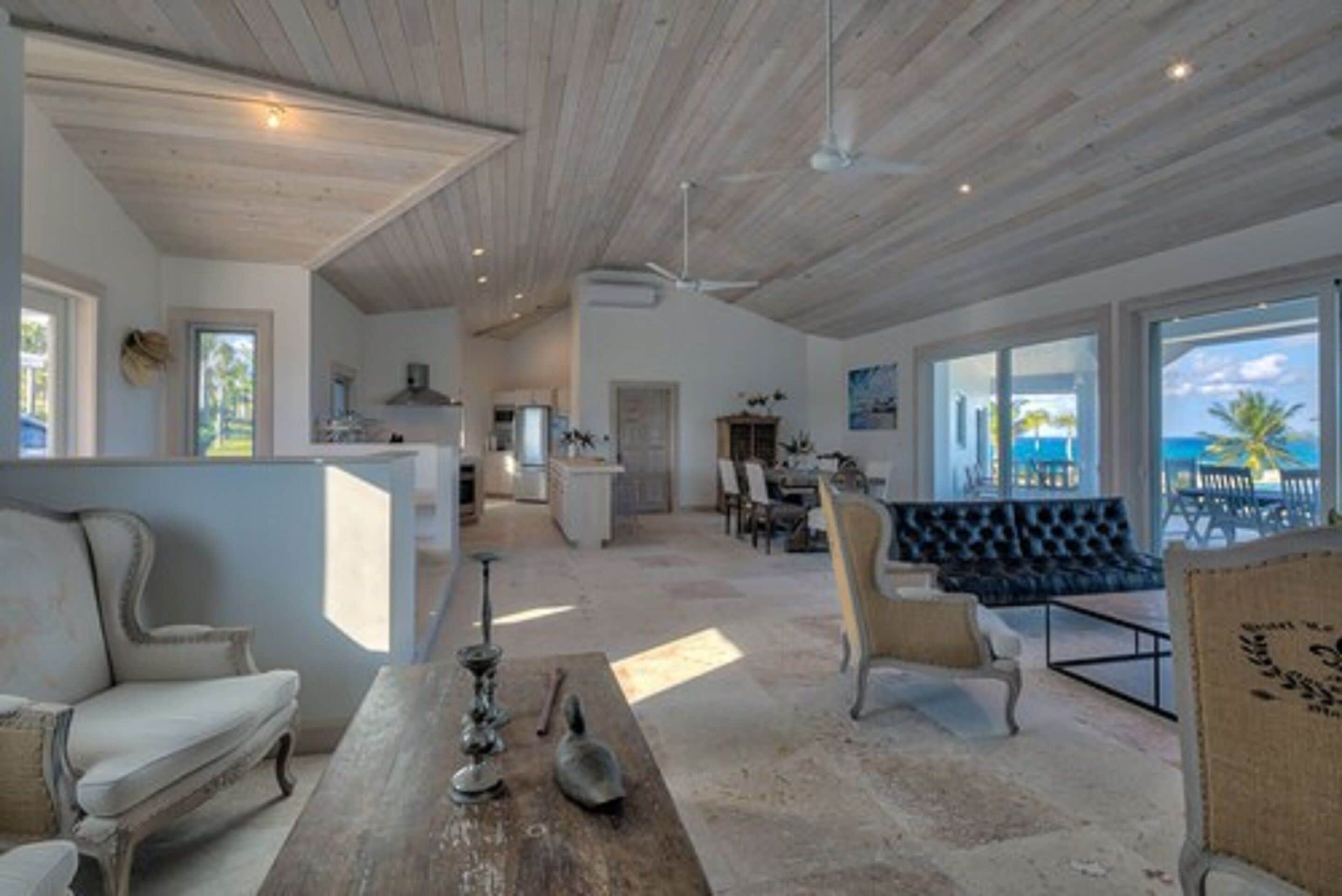 A spacious living area with a wooden ceiling, a dining area with a view, and a kitchen in the background.