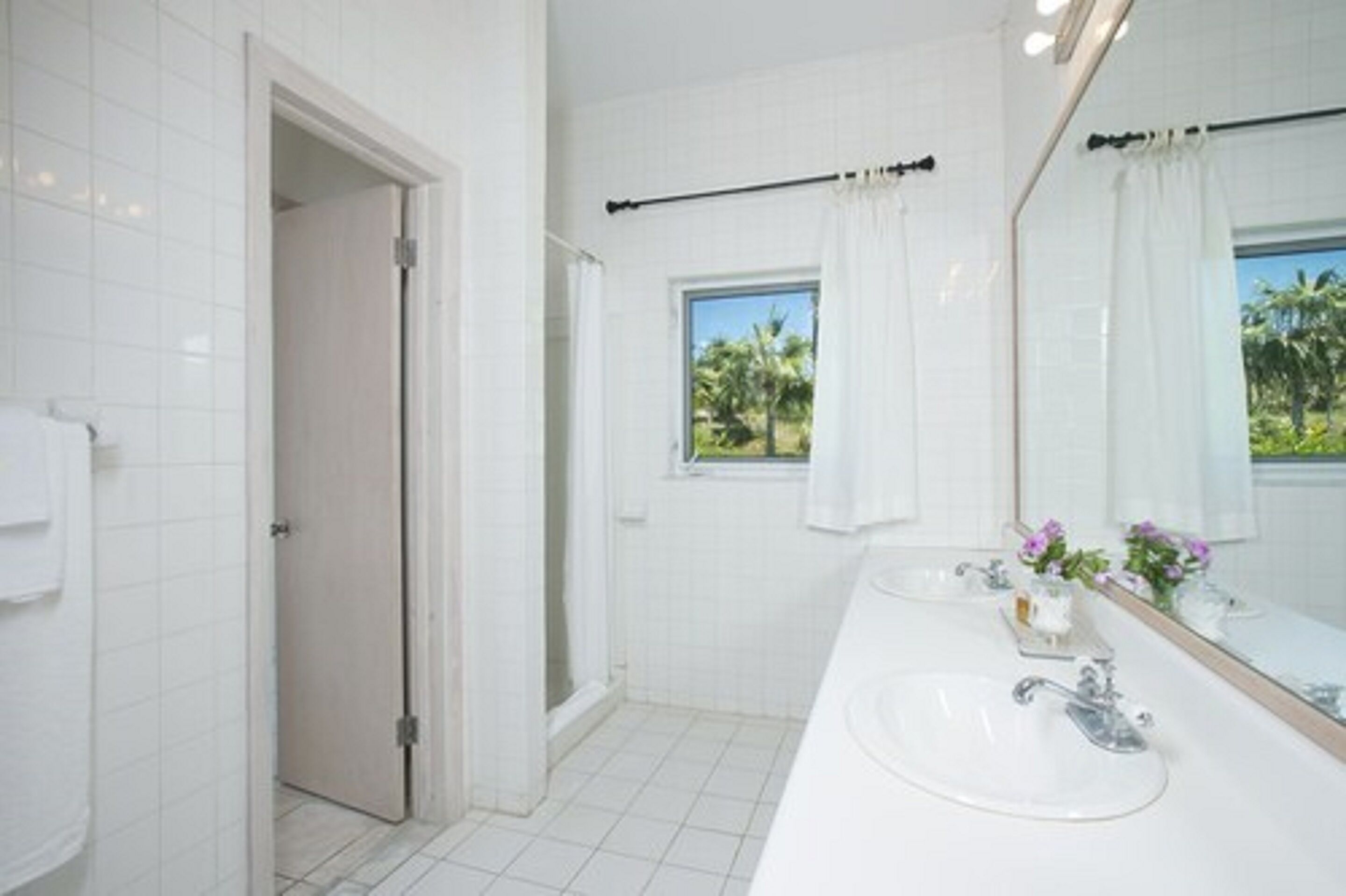 Un bagno moderno con piastrelle bianche, uno specchio grande, due lavabi e una zona doccia.