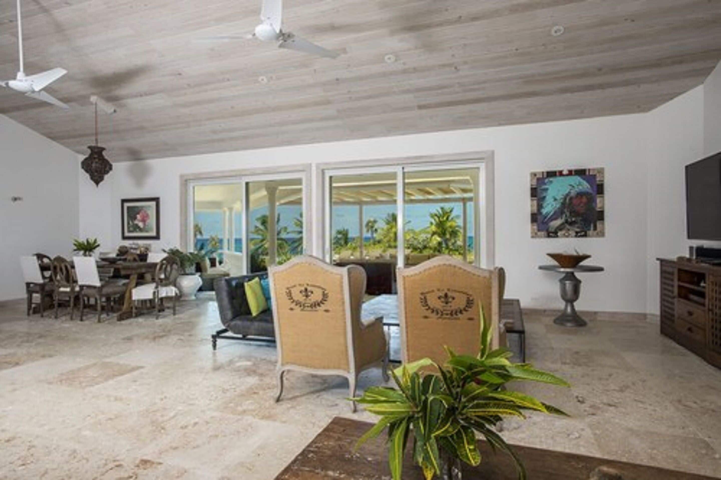 A spacious living area with a high ceiling, a dining set, and a large window offering a view of palm trees.
