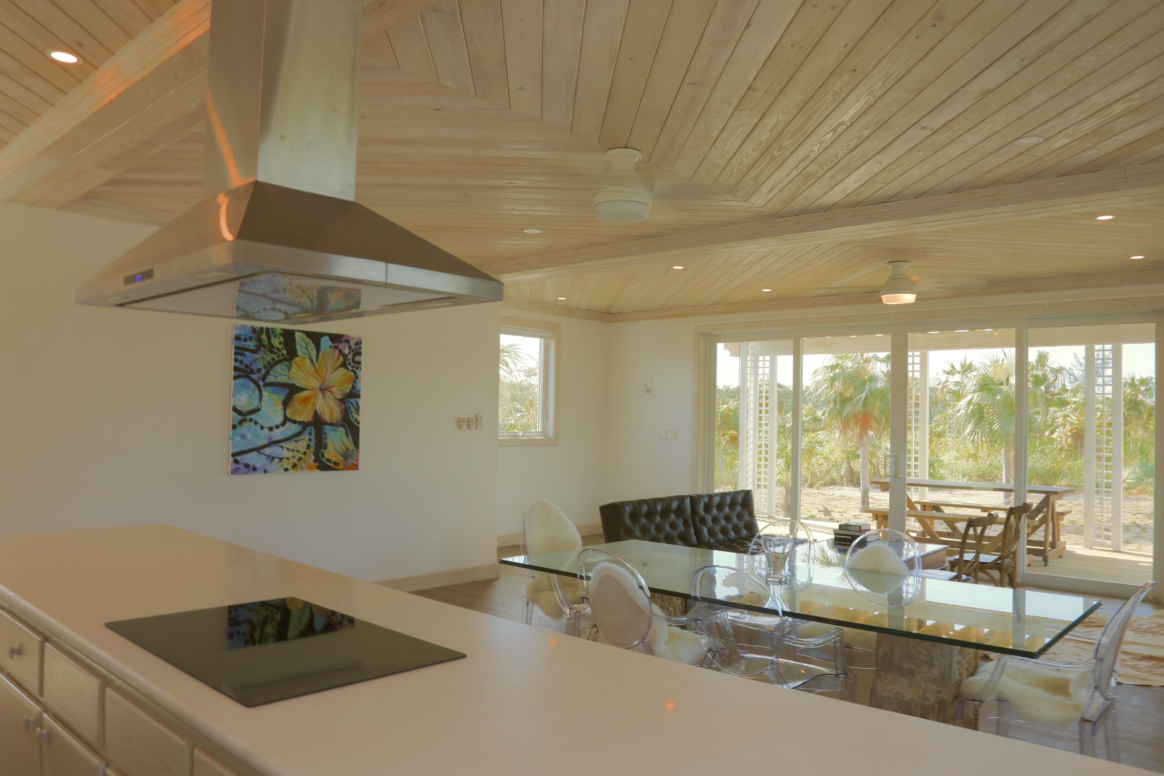 Una cocina moderna con una isla de cristal, extractor de acero inoxidable y un comedor con mesa y sillas de cristal.