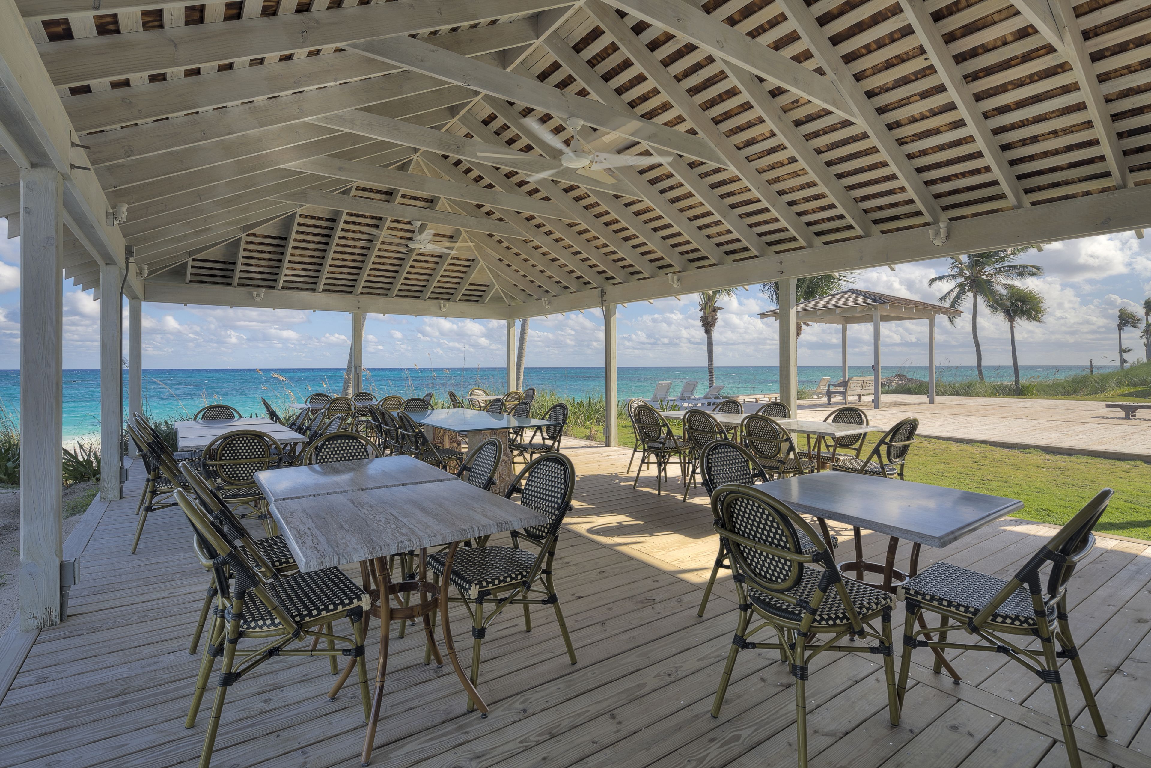 An outdoor patio with tables and chairs, overlooking the ocean.