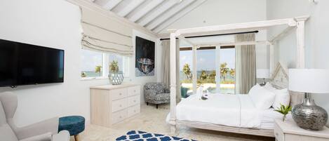 A bedroom with a large bed, a television, a chair, and a view of the outdoors.