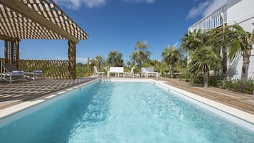 Relax by the serene pool surrounded by lush vegetation and a shaded pergola.