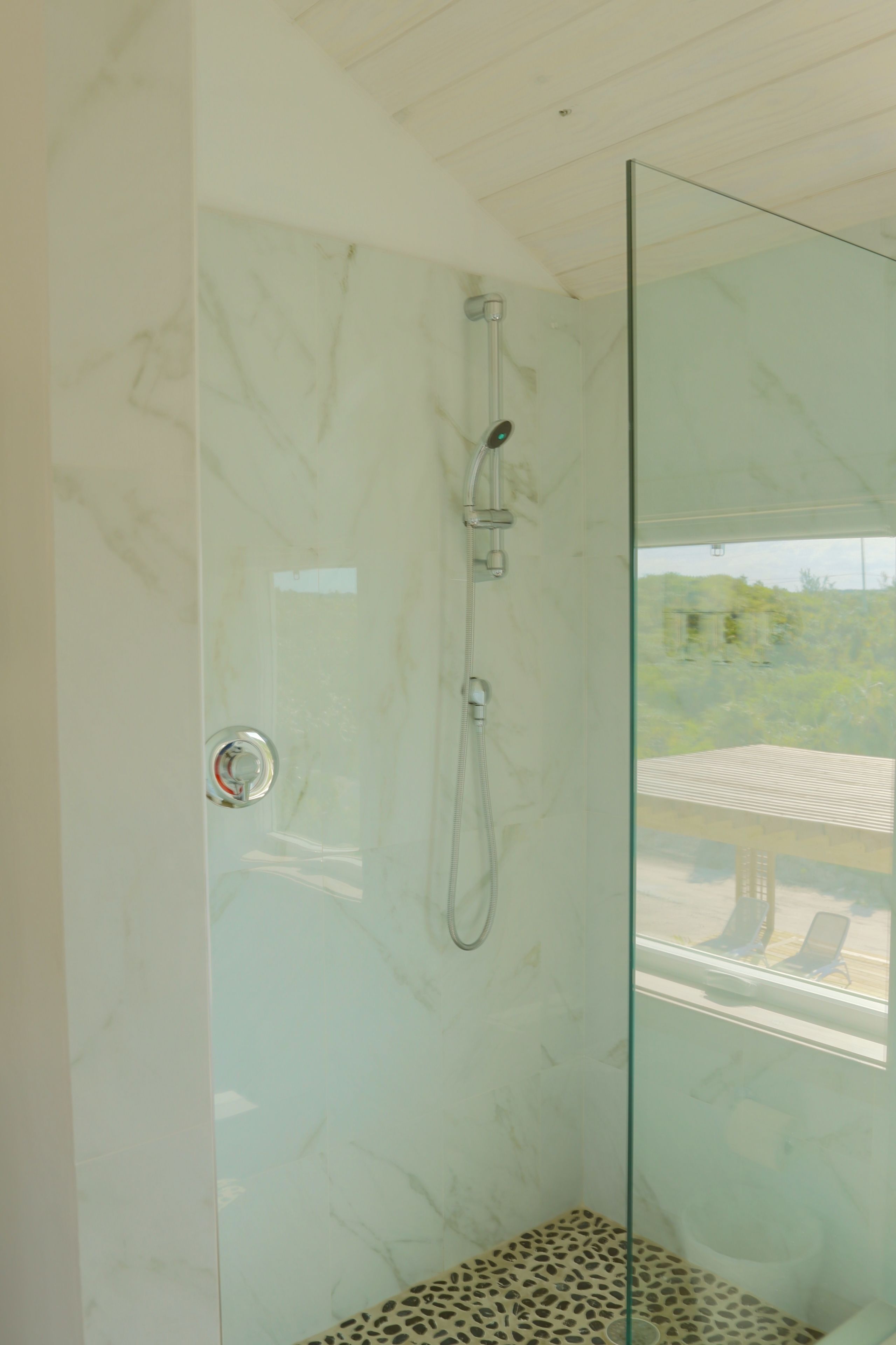 A glass-enclosed shower with a marble wall and a view of the outdoors.