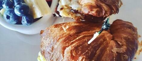 A plate with a croissant sandwich and a small bowl of fruit.
