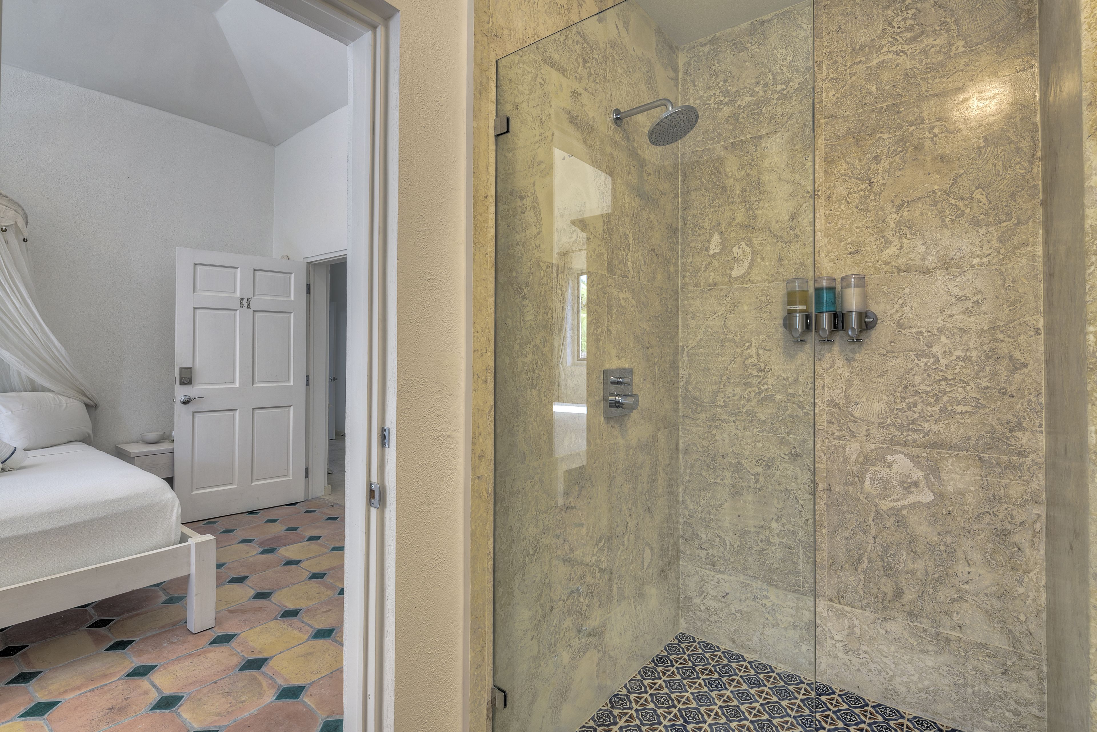 A hotel room with a bed, a shower with glass doors, and a patterned floor.