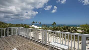 A wooden deck with white railings, a white bench, and a view of the beach and ocean.