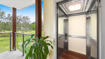 Un ascenseur doté d’une porte en verre, d’une plante en pot et offrant une vue sur un espace verdoyant à l’extérieur.