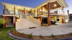 A modern two-story house with a covered front porch, a staircase leading to the upper level, and a garage with a parked car. - Ana Mandara Luxury Retreat (Port Macquarie)