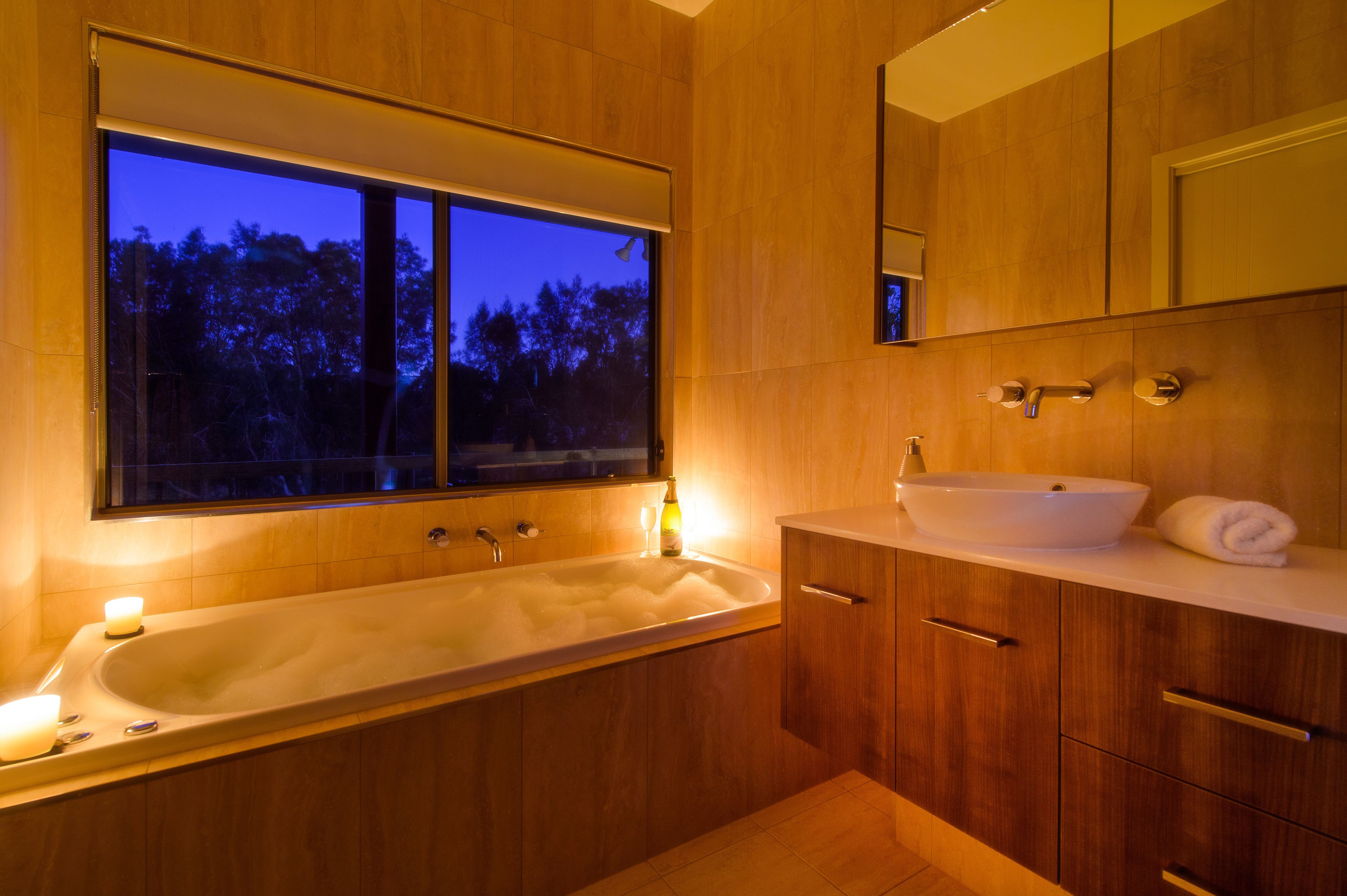 Un baño moderno con una bañera grande, un lavabo y una ventana con vistas a una zona boscosa.