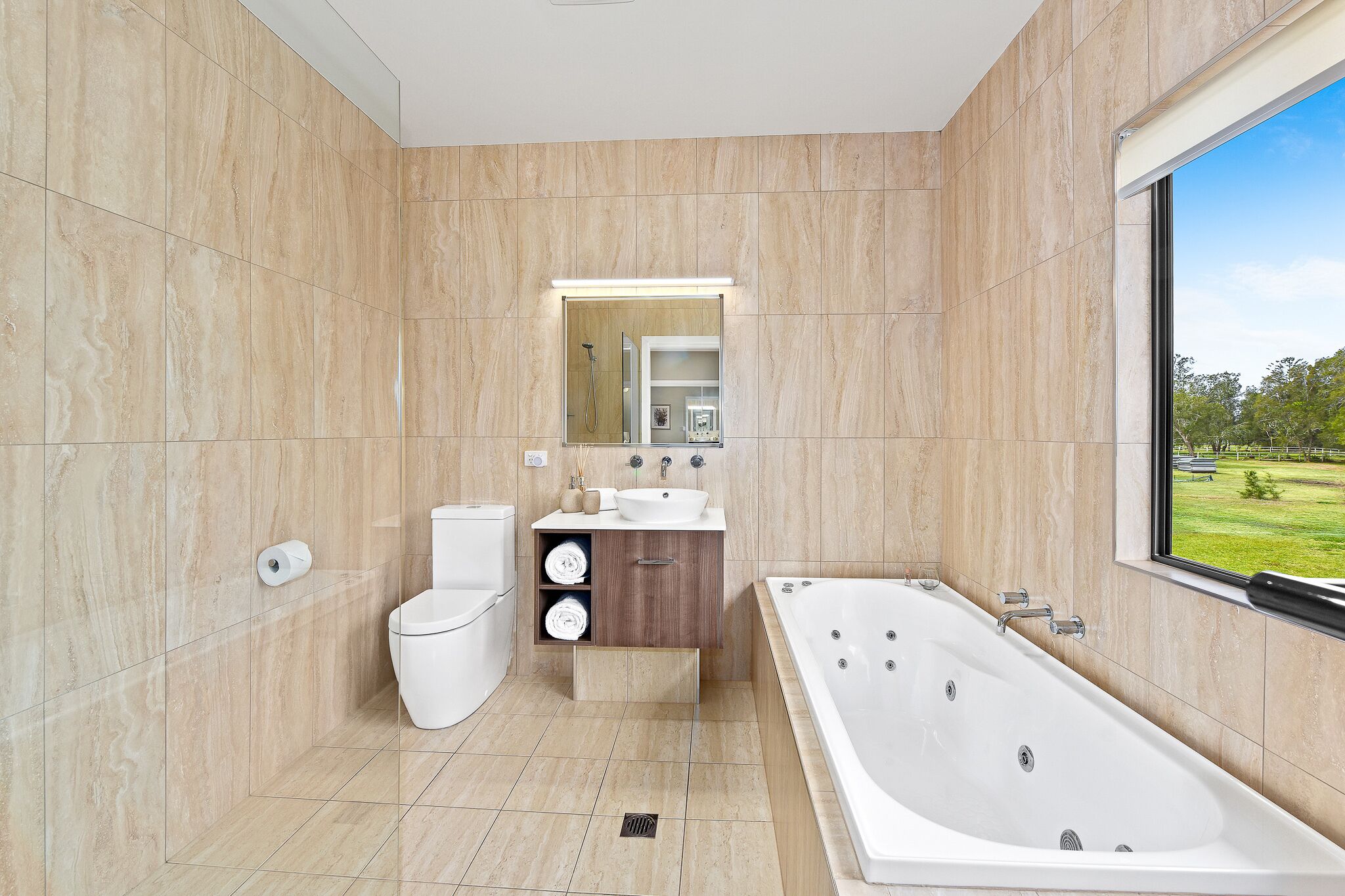 A modern bathroom with a large bathtub, a toilet, and a vanity with a sink and mirror.