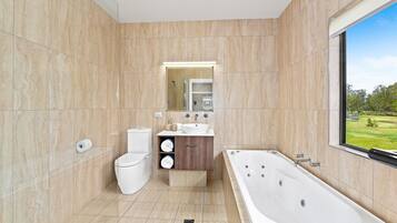 A modern bathroom with a large bathtub, a toilet, and a vanity with a sink and mirror.