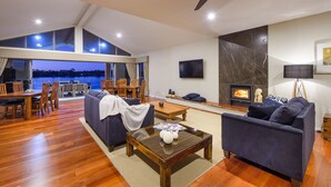 A spacious living area with a high ceiling, a fireplace, and a large window overlooking a scenic view. - Ana Mandara Luxury Retreat (Port Macquarie)
