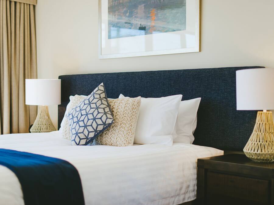 A hotel room with a large bed, two bedside lamps, and a framed picture on the wall.
