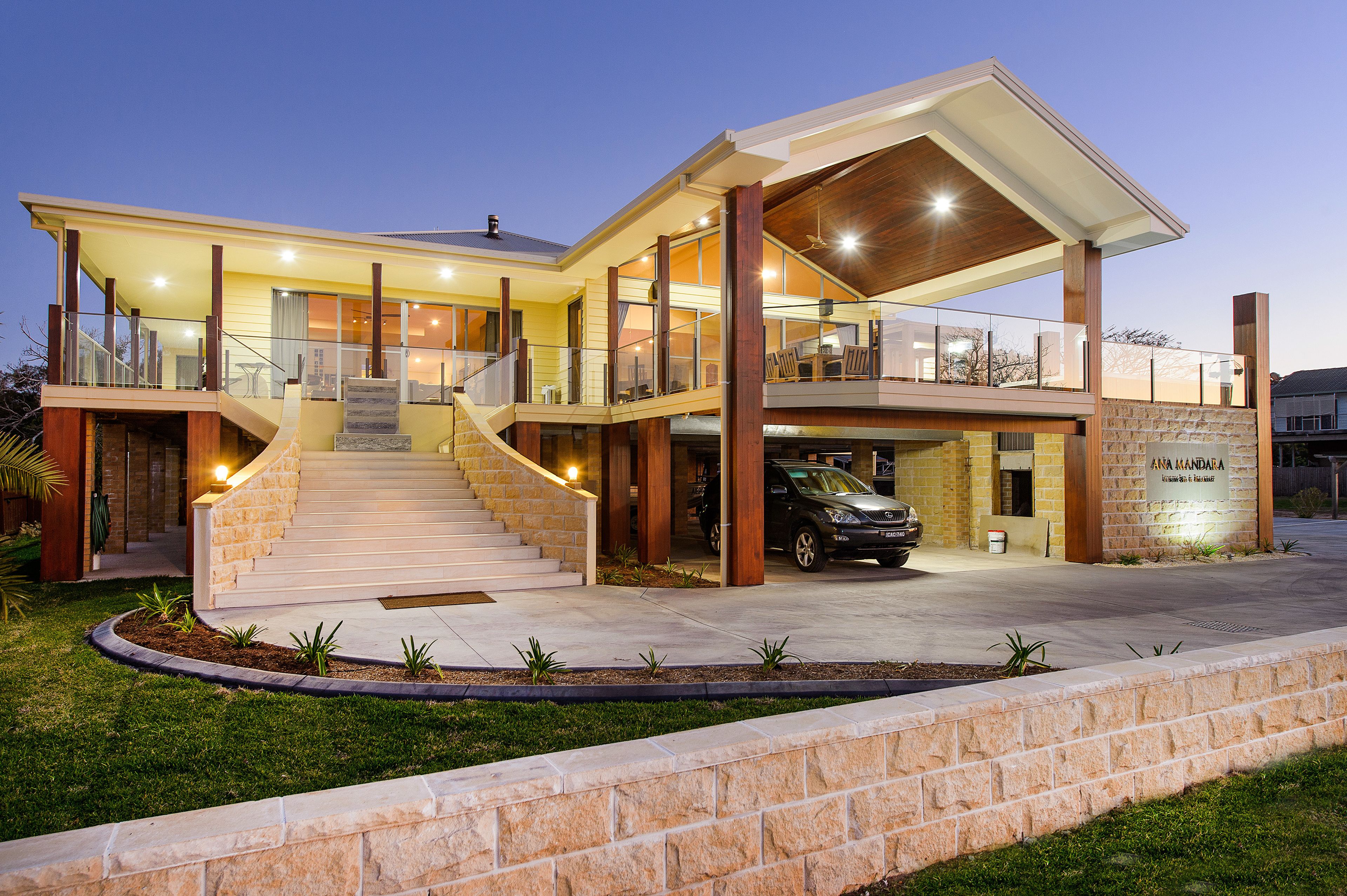 A modern two-story house with a covered front porch, a staircase leading to the upper level, and a driveway with a parked car.