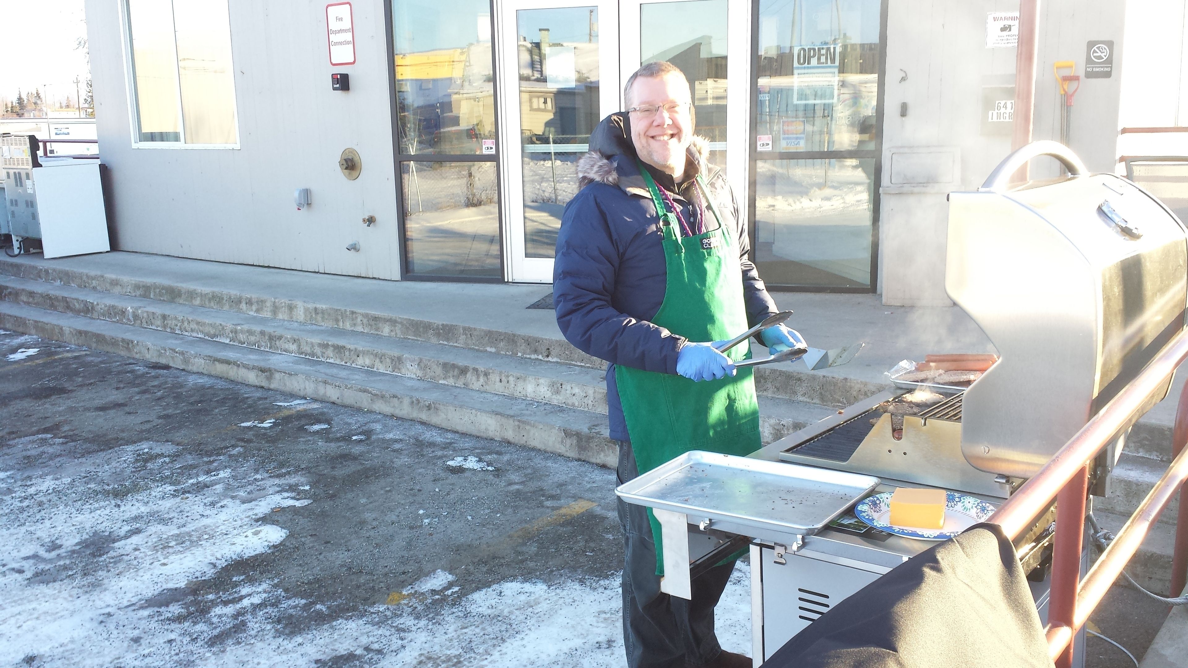 A person grilling outdoors with a portable grill, wearing a green apron and gloves.