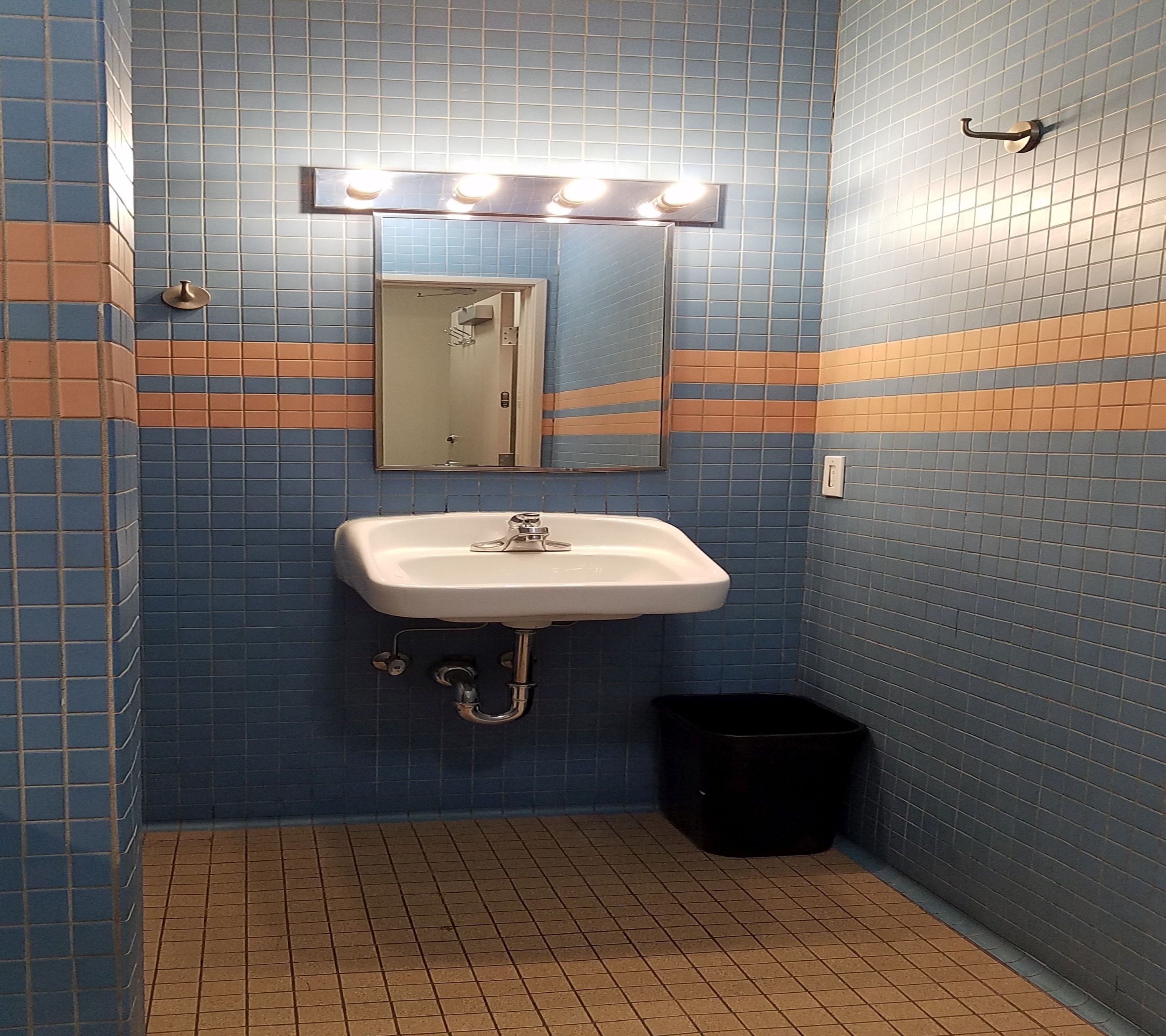 Een badkamer met een wit wastafel, blauwe betegelde wanden en een zwarte prullenbak.