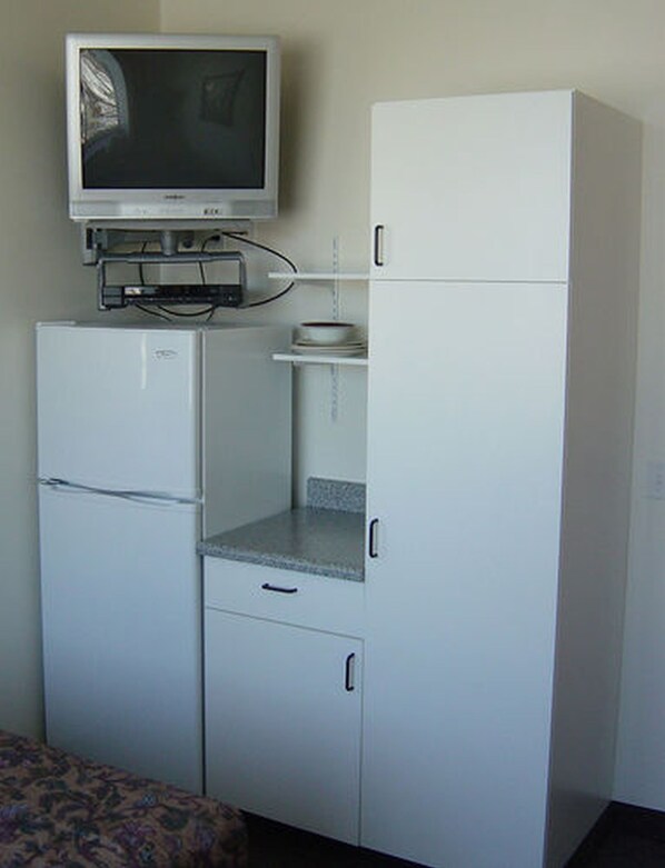 A compact kitchenette with a refrigerator, a microwave, a small countertop, and a television mounted above the fridge.