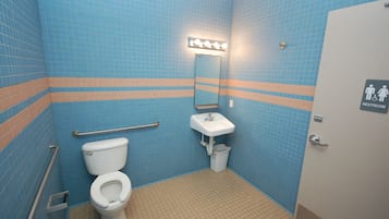 A restroom with blue tiled walls, a white sink, a mirror with lights, a handrail, and a sign indicating a handicap-accessible toilet.