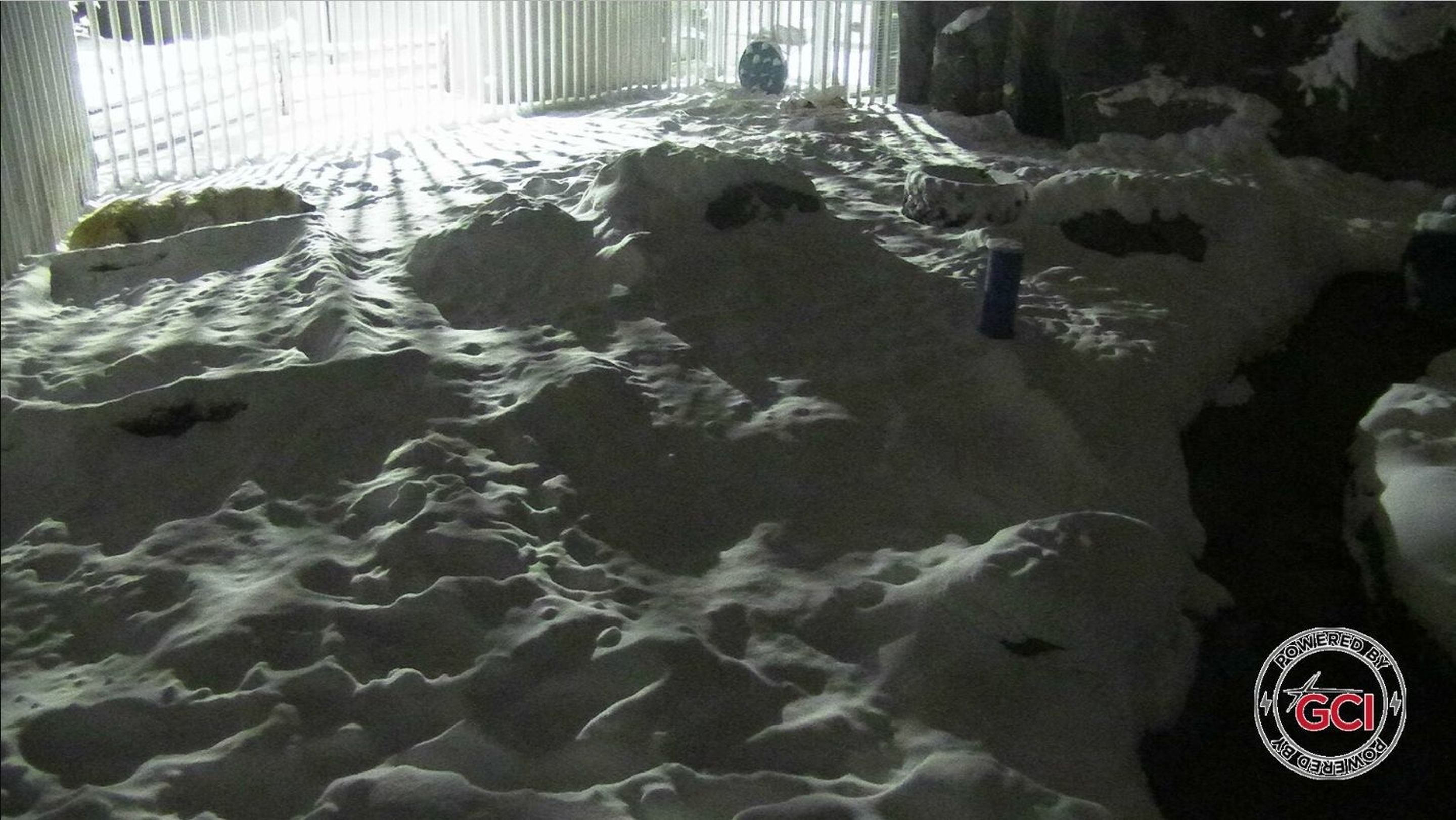A room with a large pile of snow on the floor, a window with blinds, and a logo in the corner.
