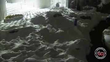 A room with a large pile of snow on the floor, a window with blinds, and a logo in the corner.
