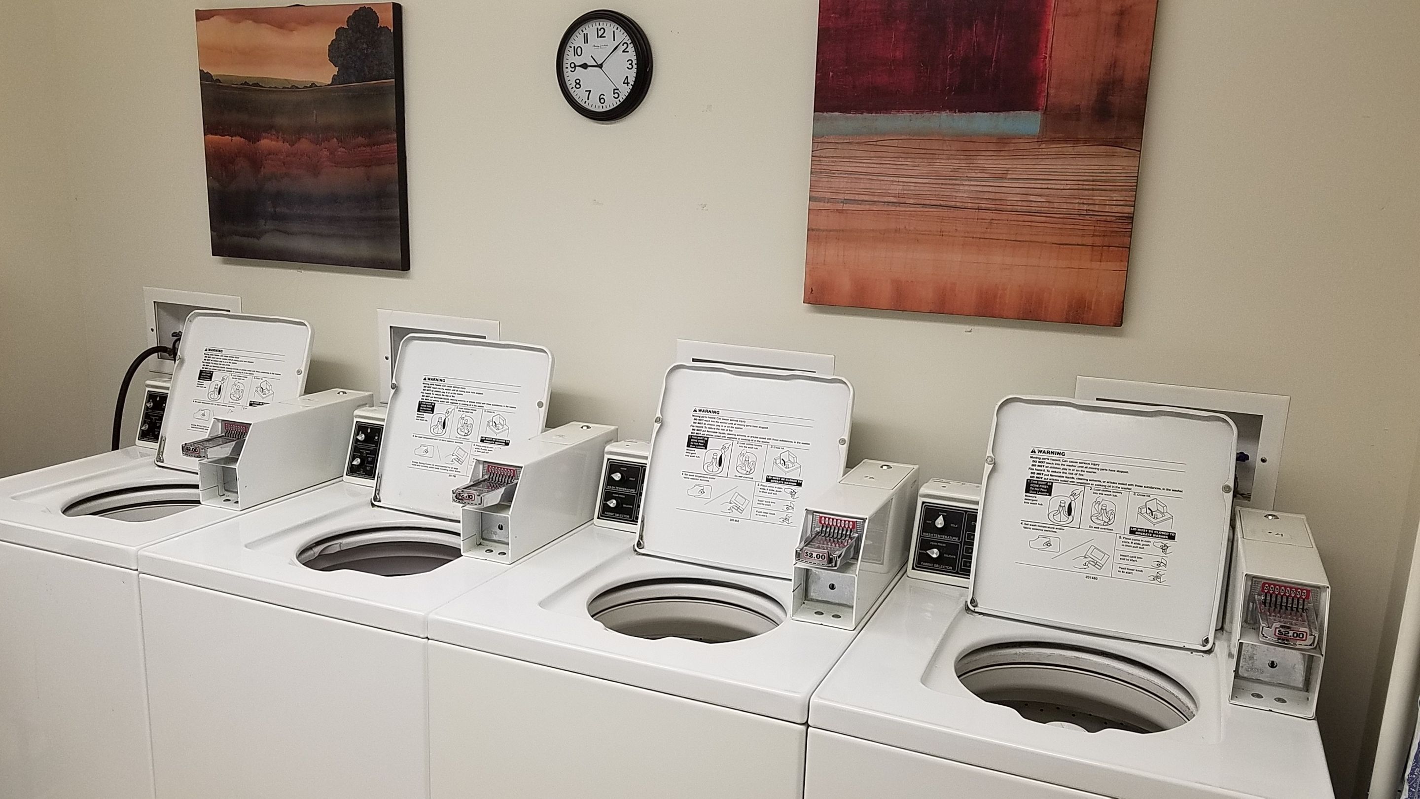 Uma fileira de sanitários públicos brancos, com pias individuais e secadores de mãos, cada um com uma etiqueta de aviso.