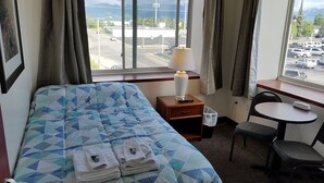 Habitación de hotel con cama, escritorio, silla, lámpara y vista al estacionamiento a través del ventanal.