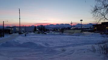A snowy parking lot with cars and buildings in the background, surrounded by mountains.
